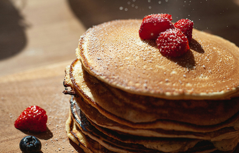 Stack of fluffy golden protein pancakes topped with fresh fruit