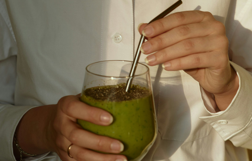 A woman holding a green smoothie in a glass, representing clean nutrition principles