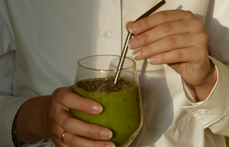 A woman holding a green smoothie in a glass, representing clean nutrition principles